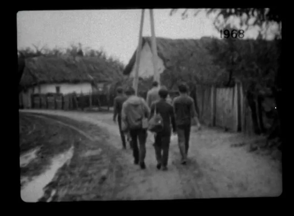 Archív filmkocka 1968-ból: férfiak sétálnak a nádtetős házak közötti falusi utcán.
